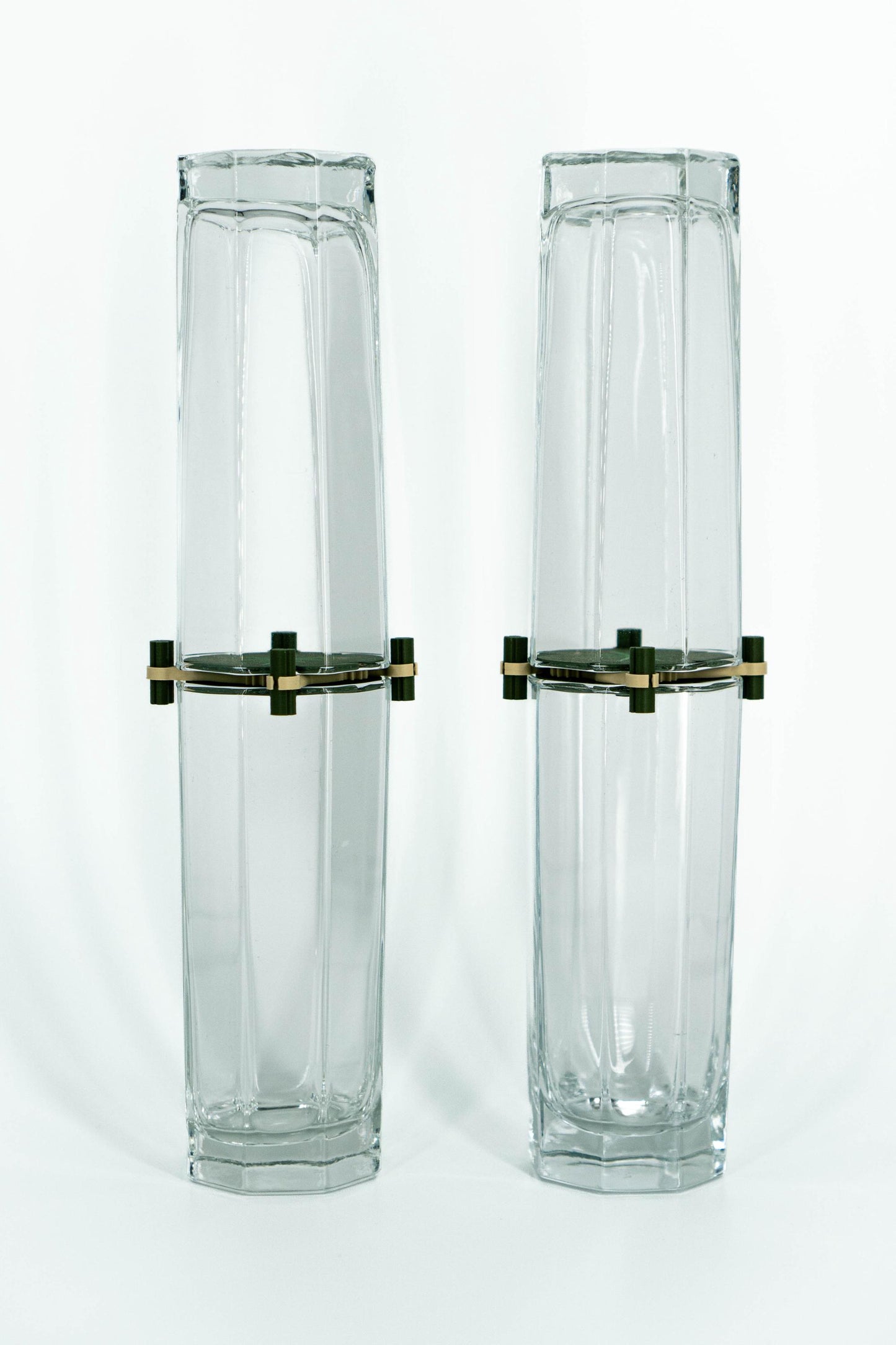 Two tall, hexagonal glass vases with brass bases on a white background