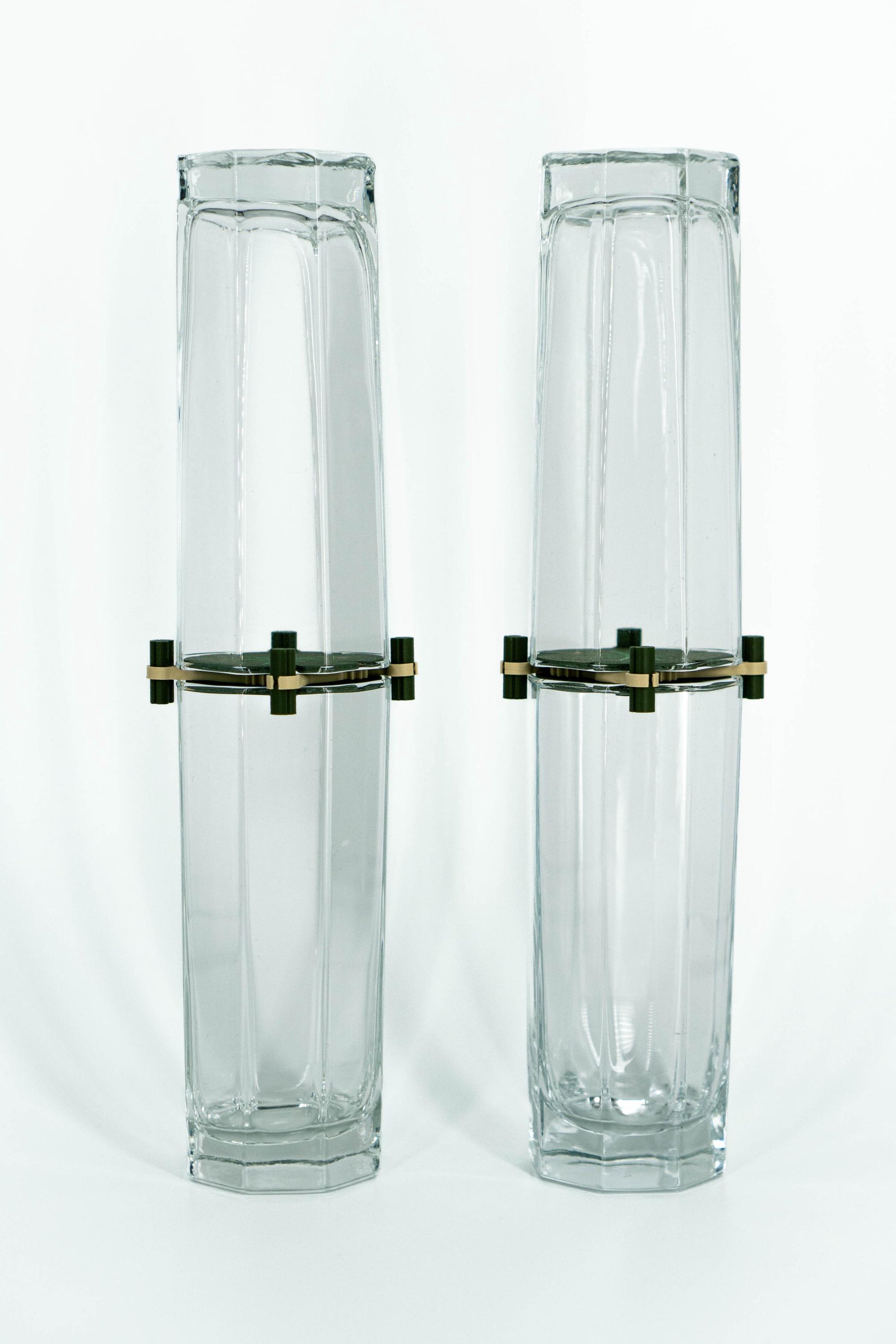 Two tall, hexagonal glass vases with brass bases on a white background