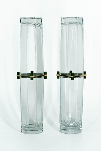 Two tall, hexagonal glass vases with brass bases on a white background